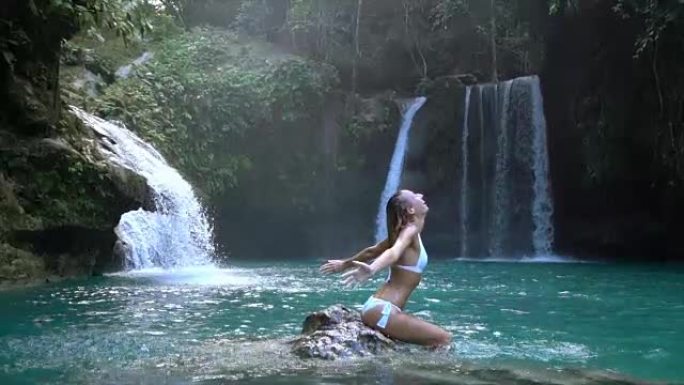 年轻女子在菲律宾宿雾岛上美丽的瀑布上在水中扔头发。人们旅行热爱自然的概念。一个人只在和平的环境中享受