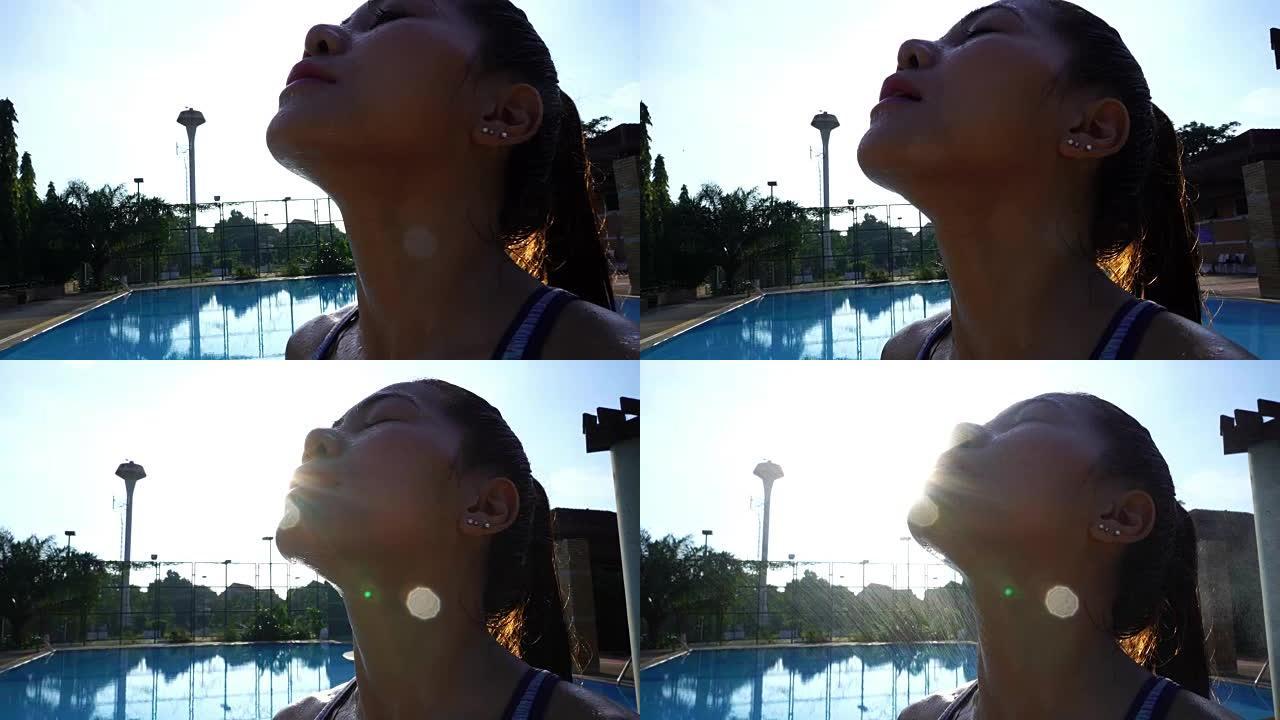 亚洲性感女人在游泳池边健身瑜伽和普拉提后喷洒新鲜矿泉水，阳光耀斑
