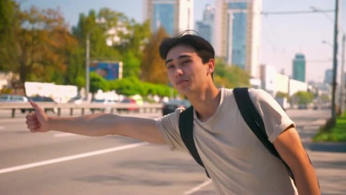 可爱的亚洲男孩在路上接车，独自站在高速公路上微笑并露出牙套，这是旅行的理想天气
