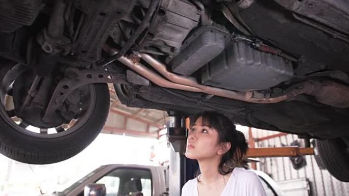 特写平移侧视图: 年轻女机械师检查车下的缺陷