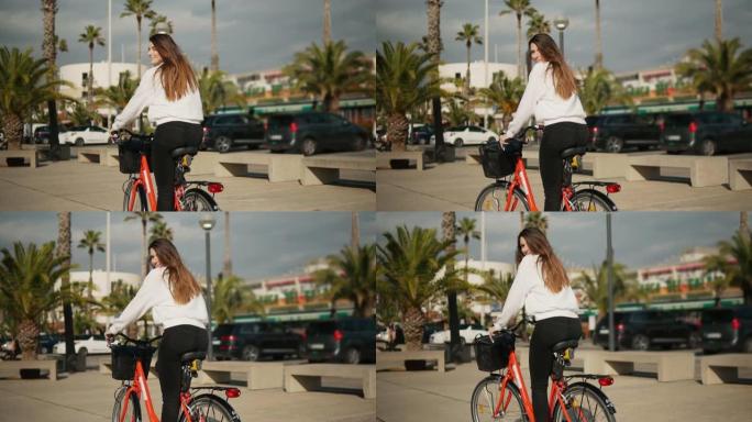 年轻女子或女孩骑自行车在棕榈树旁踩踏板