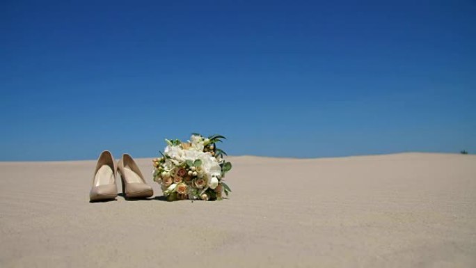 夏天，沙漠，婚礼女性米色高跟鞋站在沙滩上，在婚礼花束旁边。天，在蓝天下