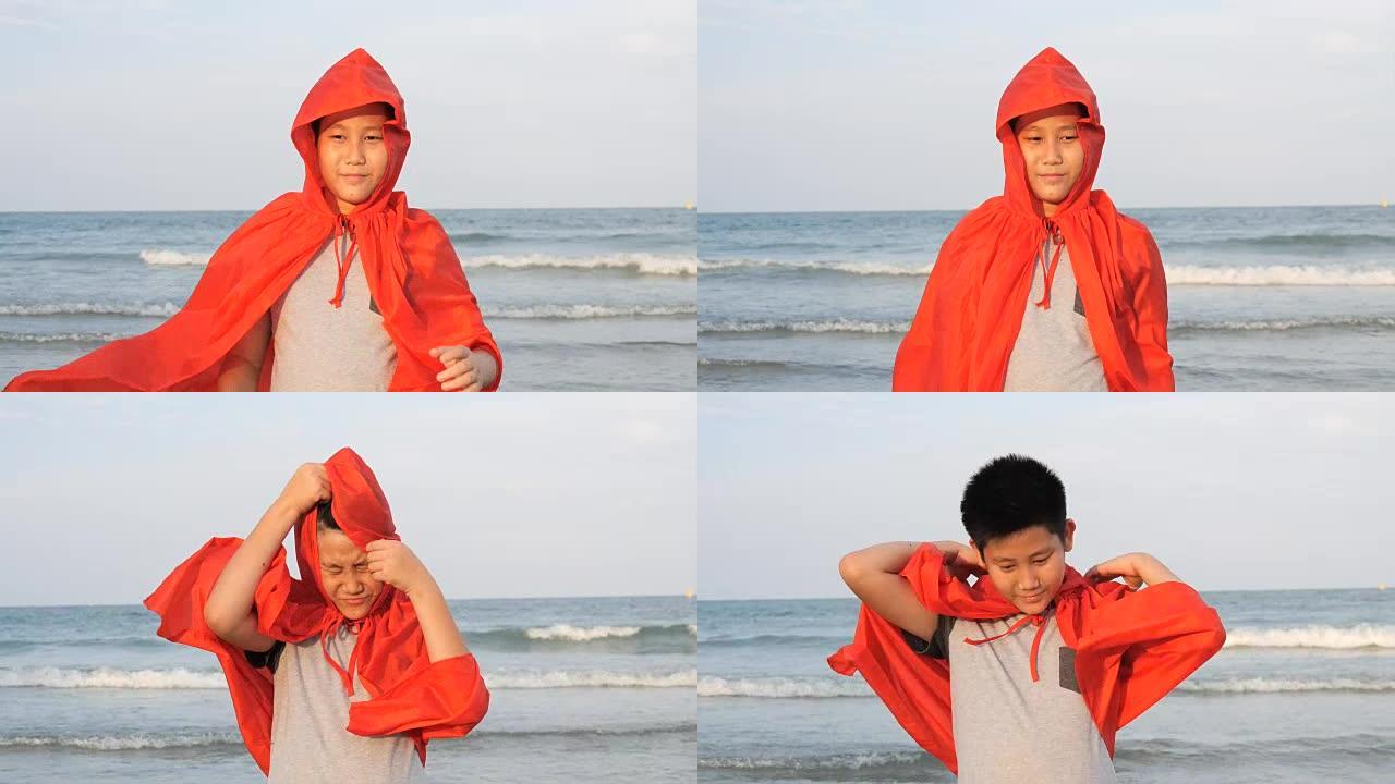 穿着红色封面的亚洲青春期男孩站在海滩上，带着超级英雄概念，慢动作。