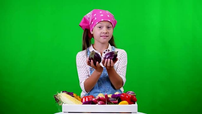 可爱，微笑，小农家女孩展示了一个装有不同新鲜蔬菜的盒子，收获。在工作室的绿色背景上。健康食品到你的餐