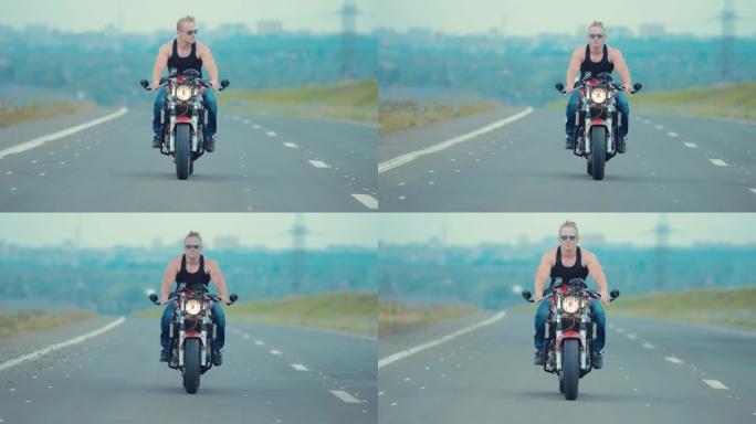 一个戴着墨镜的年轻人在柏油路上骑摩托车的前视图