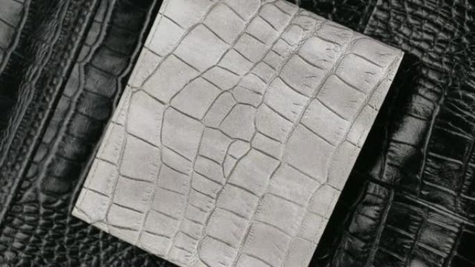 旋转，两个纹理鳄鱼皮，灰色皮革钱包躺在黑色皮肤上。特写。