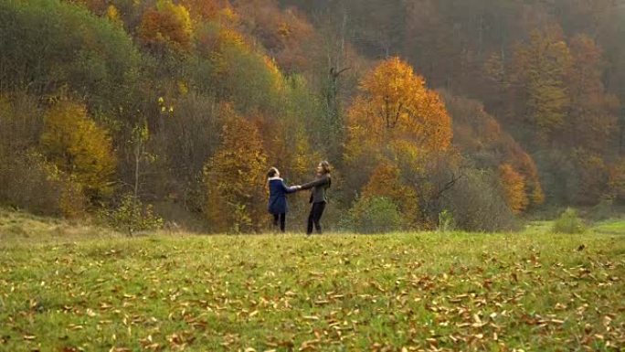 一位年轻的母亲和她的小女儿在秋天的森林里玩耍。妈妈和女儿手牵着手愉快地旋转。他们很高兴。