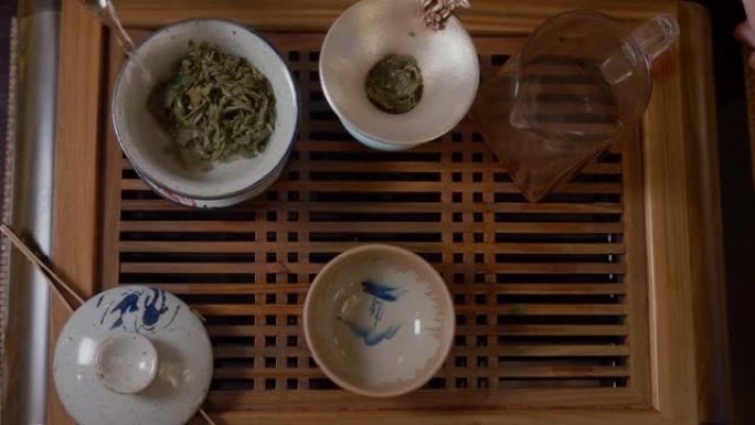 师傅在盖湾用茶壶倒热水，茶几上有绿茶