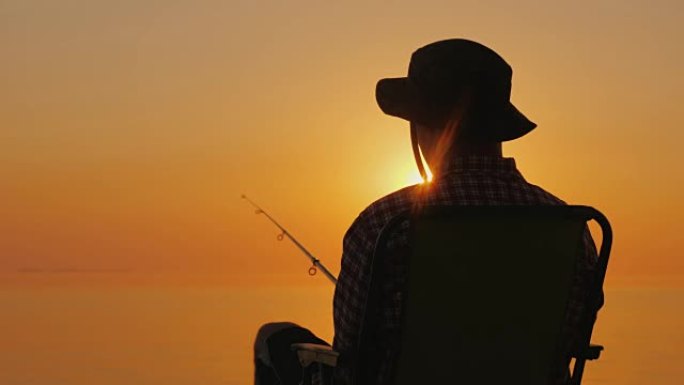 后视图-一个男人坐在海边，用钓鱼竿钓鱼