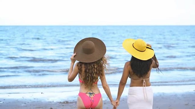穿着比基尼的快乐女人在海滩上聊天和散步
