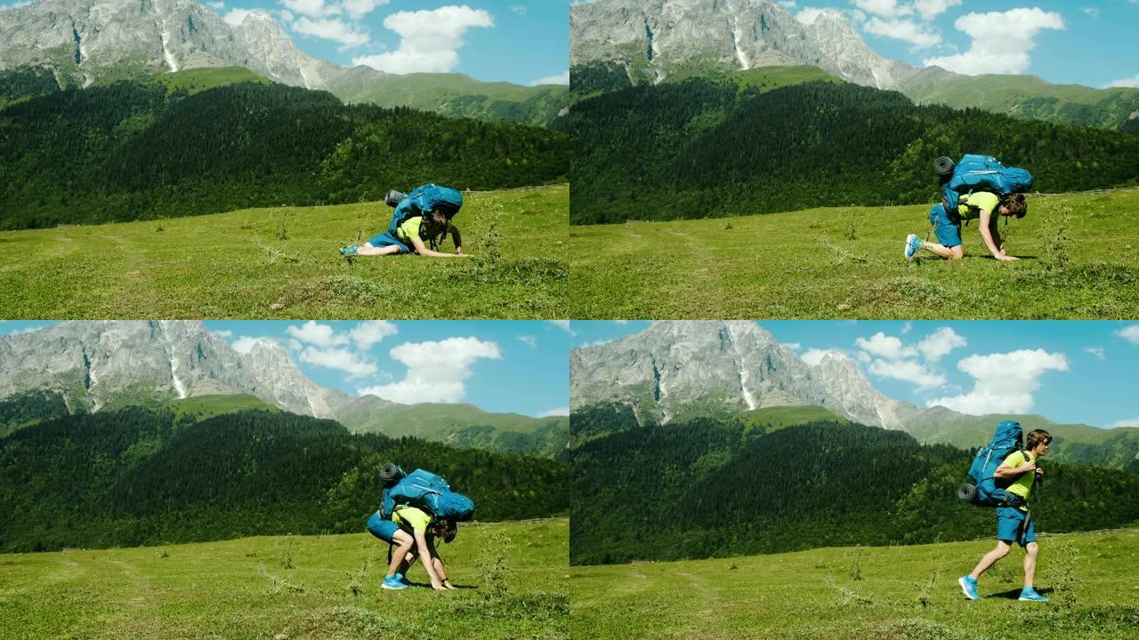 一个疲惫的游客带着一个大背包从地上爬起来，在美丽的山景背景下徒步旅行，一个病人慢慢站起来走路