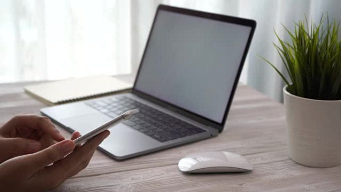 年轻女子在家工作时使用智能手机和笔记本电脑放在桌子上，女人的手使用智能手机技术，