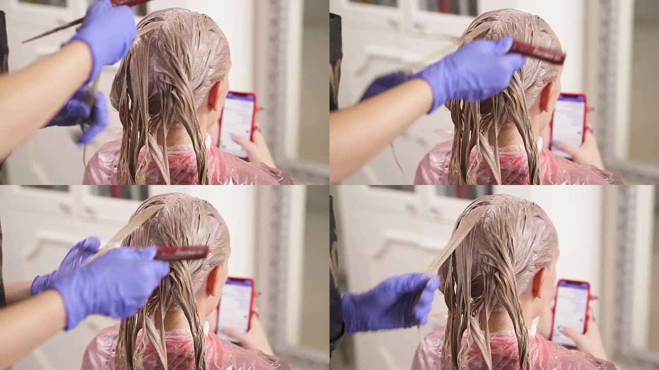 一个染发的女人坐在镜头前。美发师取一股，用鼠尾梳的手柄将其拉伸。该名女子拿着电话并输入消息。