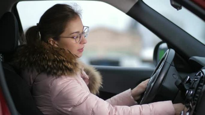 穿着夹克和眼镜的女孩坐在车里，启动它，离开4k慢动作