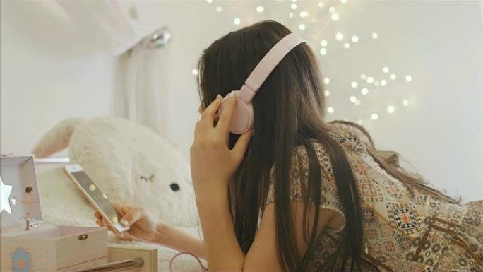 漂亮的白人女孩在床上用耳机和智能手机听音乐，4k