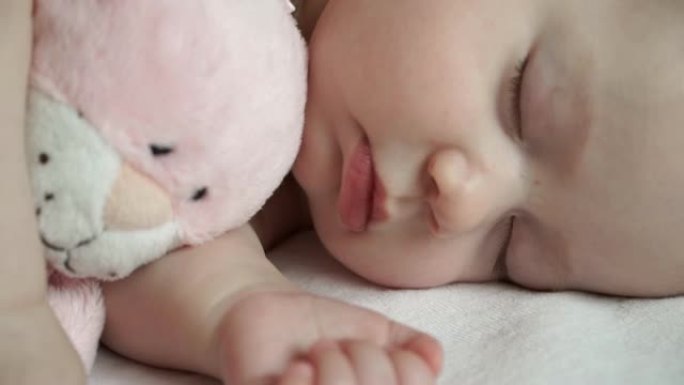 一个可爱的新生女孩用柔软的粉红色猫玩具甜蜜睡觉的特写镜头