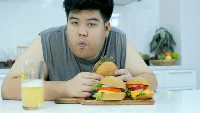 超重的年轻人在桌子上寻找快餐，吃大汉堡