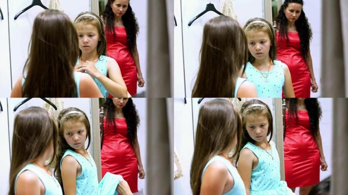 购物。在大型商店的试衣间里，一个漂亮，严肃的女孩，一个孩子试穿新衣服，选择买什么。镜子里的反射。童装