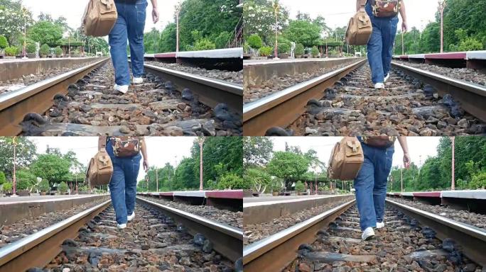 穿着牛仔裤在铁轨上提着行李的妇女。她绊倒了，但仍然向前走。构思，旅行，努力奋斗