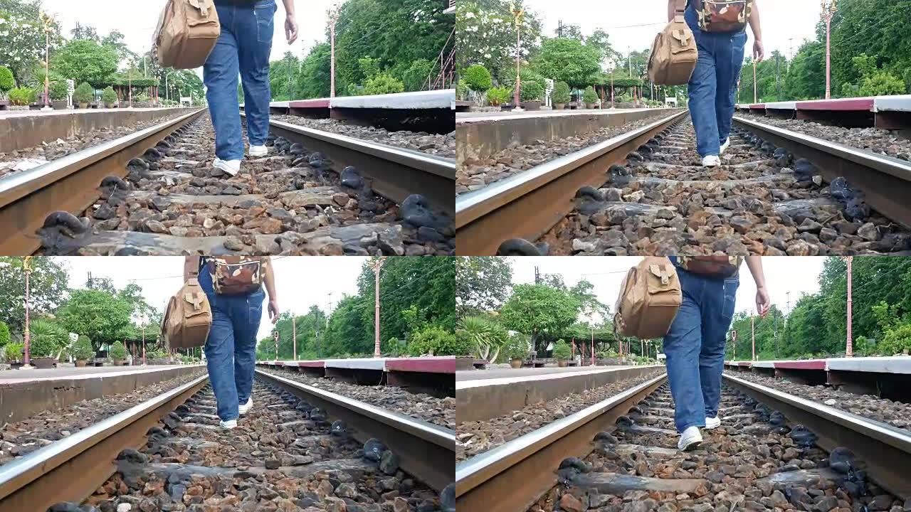 穿着牛仔裤在铁轨上提着行李的妇女。她绊倒了，但仍然向前走。构思，旅行，努力奋斗
