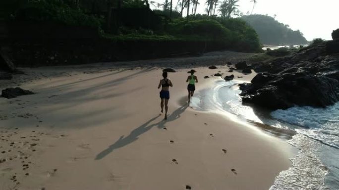 早上日出时，两个健康生活方式的年轻女性朋友在热带海滩上奔跑，航拍