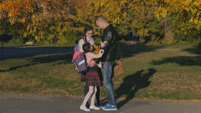 年轻快乐的父亲在学校遇见了他的女儿。两个和爸爸穿校服的女孩。慢动作秋季日落