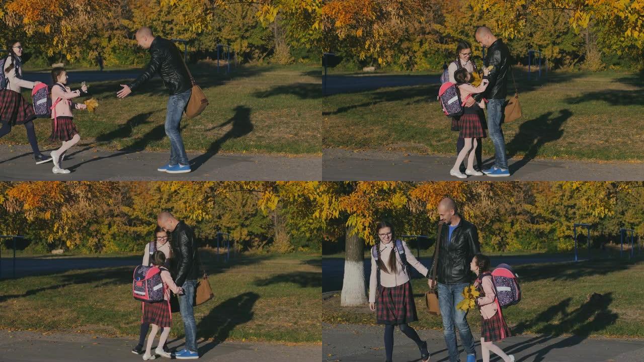 年轻快乐的父亲在学校遇见了他的女儿。两个和爸爸穿校服的女孩。慢动作秋季日落