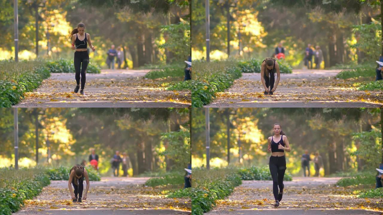 穿着连身衣的年轻女孩，在秋公园里奔跑着耳机，停下来系她的士力架，继续慢跑。