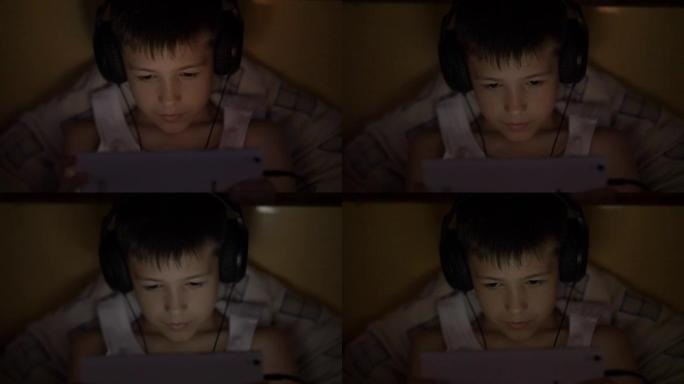 男孩在平板电脑上使用，躺在家里戴着耳机，在视频通信上进行对话，玩游戏