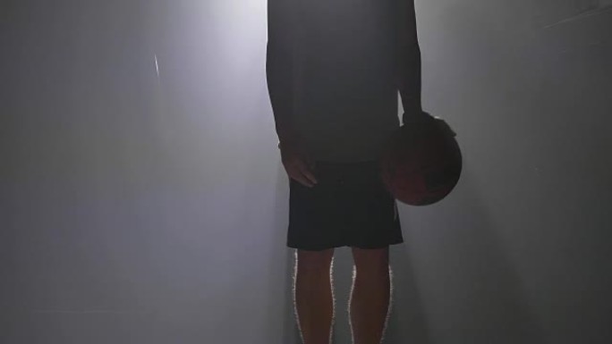 用泛光灯在迷雾的房间里近距离拍摄男子的双腿运球