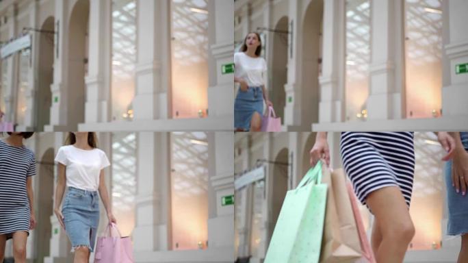 两个漂亮的女孩在购物和聊天期间慢动作地沿着时尚购物中心行走