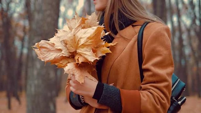 女孩手里拿着一束秋叶。特写