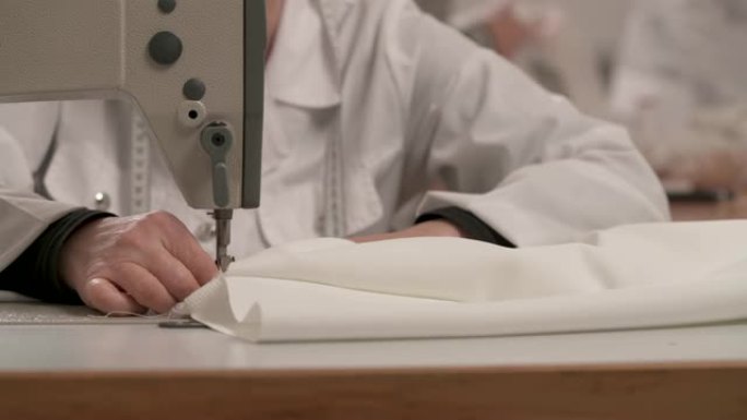 裁缝的双手在缝纫机上包边白布做婚纱的特写。工作室里的婚纱制作。
