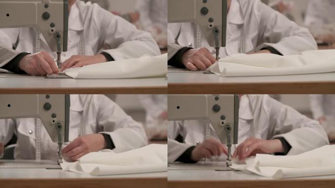 裁缝的双手在缝纫机上包边白布做婚纱的特写。工作室里的婚纱制作。