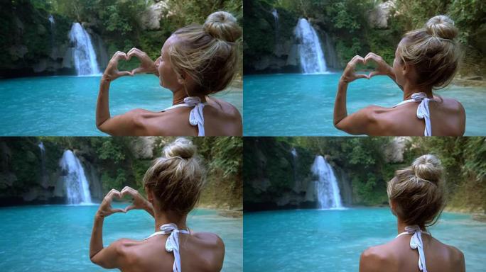 年轻女子喜欢美丽的瀑布，在菲律宾宿雾岛上制作心形手指框架。人们旅行热爱自然的概念。一个人只在和平的环