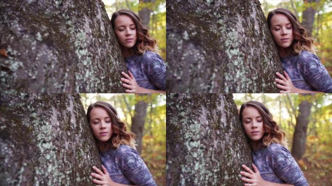 美丽的女人闭着眼睛拥抱大树的滑动视图。秋天