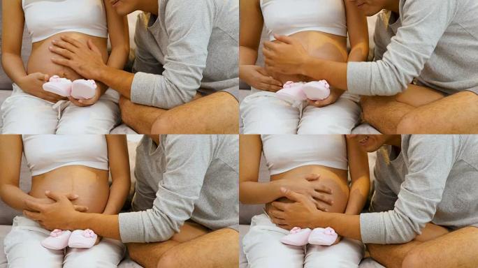 美丽的孕妇和她的丈夫在家里的沙发上抱着和听肚子里的婴儿，怀孕和家庭观念