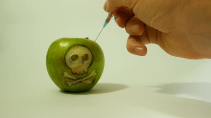 注射器插入带有雕刻头骨的青苹果中，代表食品，蔬菜和水果中使用转基因物质的形象