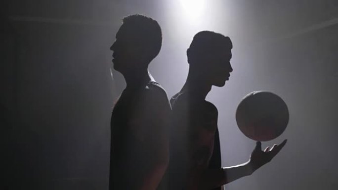 两名篮球运动员的剪影背靠背站在房间里，烟雾和泛光灯