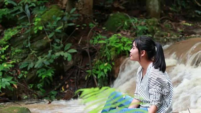亚洲年轻女孩坐在热带雨林绿树蕨附近放松，在自然公园的水落。
