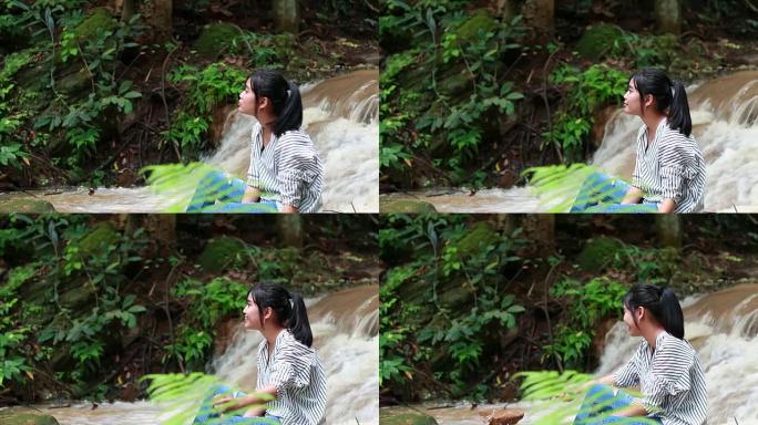 亚洲年轻女孩坐在热带雨林绿树蕨附近放松，在自然公园的水落。