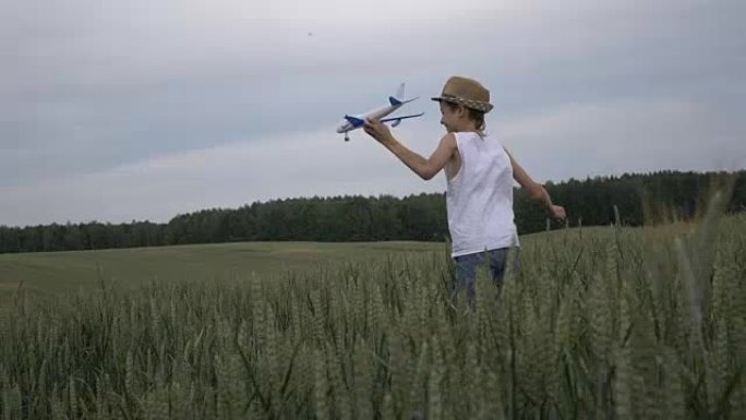 戴着草帽的快乐男孩梦想家手持飞机在户外穿越田野