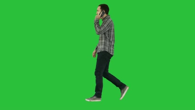 年轻的大胡子男人在绿色屏幕上在手机上走路和说话，色键
