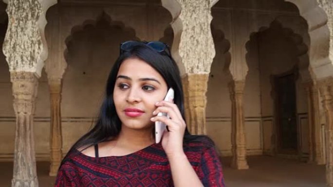 手持拍摄的年轻女子在她的手机智能交流谈话触摸屏谈话信息文本分享网络微笑在印度建筑柱拱前的背景接近
