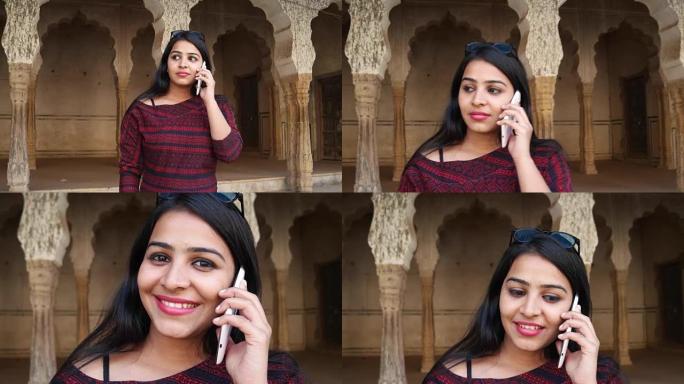 手持拍摄的年轻女子在她的手机智能交流谈话触摸屏谈话信息文本分享网络微笑在印度建筑柱拱前的背景接近