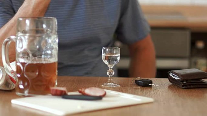 手持一杯伏特加的男性双手特写。桌子上是一杯啤酒和切成薄片的香肠。男子喝酒拿驾照
