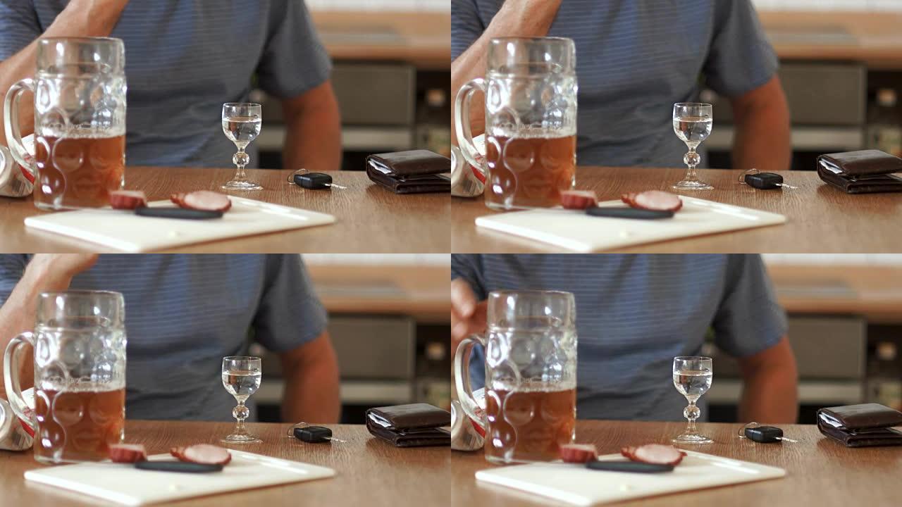 手持一杯伏特加的男性双手特写。桌子上是一杯啤酒和切成薄片的香肠。男子喝酒拿驾照
