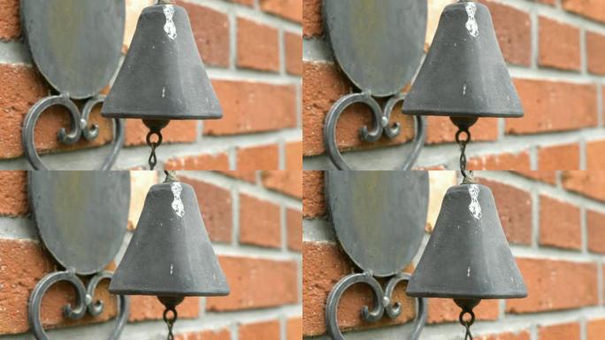 一个古老的，古老的，生锈的铃铛挂在砖墙上。敲击挂在入口处墙上的铃铛。