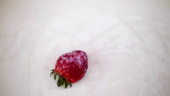 一颗红草莓浆果以慢动作落入牛奶中。