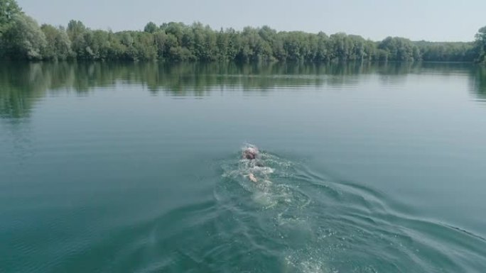 慢动作: 铁人铁人三项运动员男子训练的空中镜头。男子在铁人三项比赛的湖泊训练中游泳的无人机射击